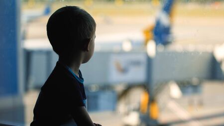 Toned portrait of sad little boy looking through window on big airplane in airport