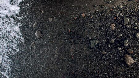 Closeup image of wet black volcanic sand and pebbles on ocean beachの写真素材