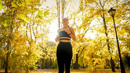 Portrait of beautiful sporty woman jogging and exercising in autumn parkの写真素材