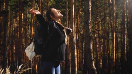 Toned phtoo of young woman travelling in forest stretching hands and enjoying warm sun light. Concept of freedom and harmony with nature.の写真素材