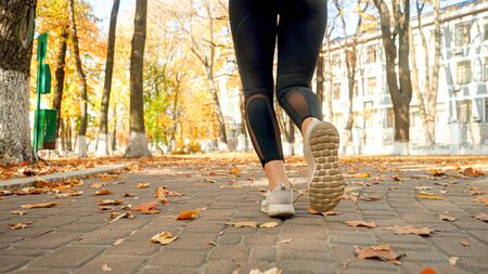 Closeup photo of female feet in sneakers jogging in autumn park