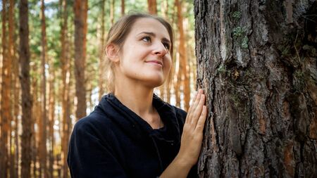 beautiful young woman with long hair touching and looking on big old pine tree. Concept of ecology, environment protection and harmony with natureの写真素材