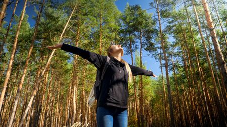 Portrait of smiling female tourist stretching hands and enjoying morning in pine tree forest