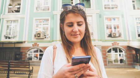 Toned portrait of young girl with smartphone against old building on city street