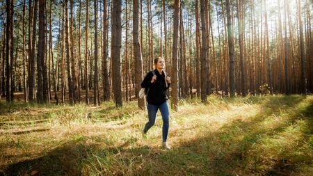 Beautiful female hiker with backpack walking out of the forest on the meadowの写真素材