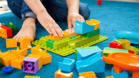 Closeup image of little toddler boy sitting on carpet at home and playing with colorful constructor blocksの写真素材