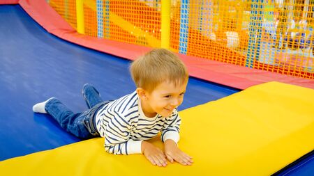 Portrait of happy laughing little boy lying on tramploine at amusement parkの写真素材