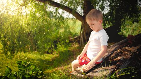 Little boy sitting at the lake and feeding ducks with breadの写真素材