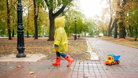 Little boy with toy truck in autumn park on rainy dayの写真素材