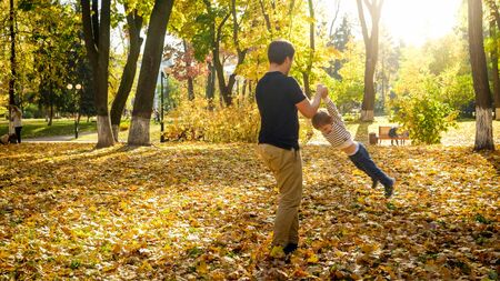 Young father holding his son by hands and spinning in autumn park.の写真素材