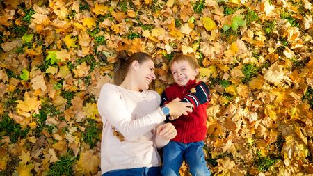 Portrait of laughing and smiling boy with young mother lying on leaves at autumn park