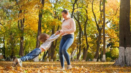 Young msiling woman holding her son by hands and spinning him at autumn parkの写真素材