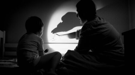 Black and white photo of mother and her child playing with shadows and flashlight on wall at bedroom.の写真素材