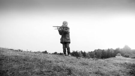Black and white image of smiling little boy standing on hill top and throwing toy aitplaneの写真素材