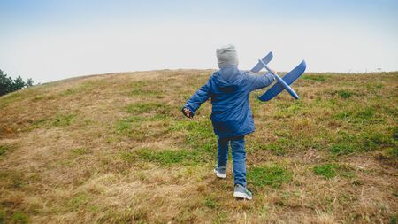 Toned photo of little boy with toy airplane running on the hill at fieldの写真素材