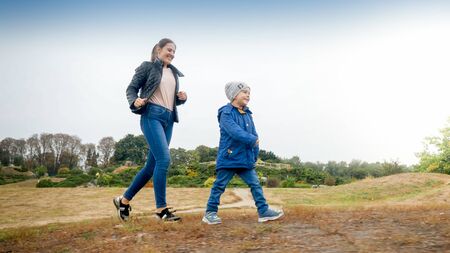 Happy smiling little boy with young mother walking on the field at autumn parkの写真素材