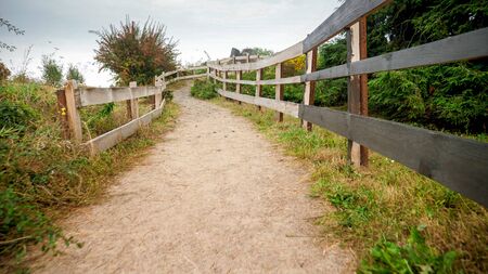 Beautful narrow path in the hills with long wooden fence on cloudy dayの写真素材