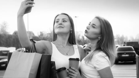 Black and white portrait of two sexy girls with shopping bags making selfie photo on shopping mall car parkingの写真素材