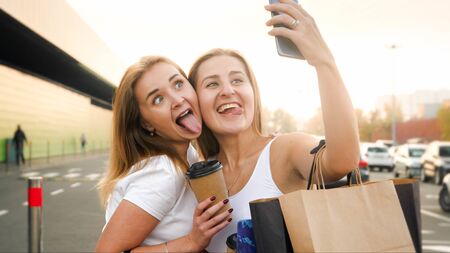 Portrait of two funny girls making face and having fun while making selfie photo of mobile phone at shopping mallの写真素材