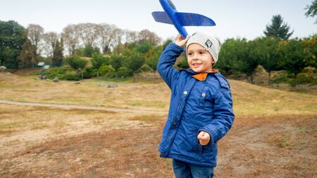 Portrait of smiling little boy throwing blue toy airplane in the fieldの写真素材