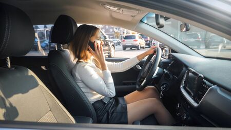 Young female driver talking by phone while looking for parking olace. Phone conversation distract...