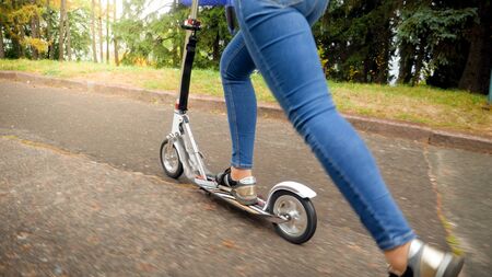 Closeup image of young woman riding fast on kick scooter at park