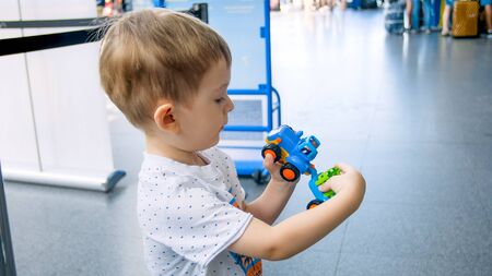 Portrait of cute toddler boy playing with toy car in modern airport terminal while waiting for flightの写真素材