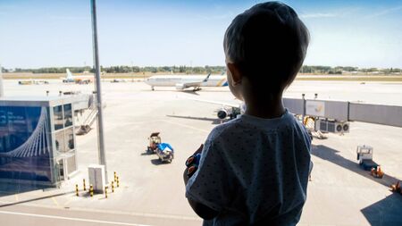 Silhouette of little boy looking on airport runway through windowの写真素材