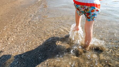 Closeup image of child's feet running in sea water on beach.