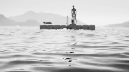 Black and white image of people resting on the floating platform in the sea.の写真素材
