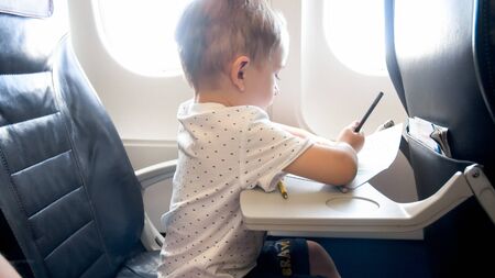 Cute little boy drawing picture with pencils while flying in airplane.の写真素材