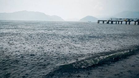 Heavy rain over the sea beach and wooden pierの写真素材