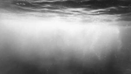 Black and white image of sun rays and floating air bubbles in sea water.の写真素材