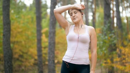 Portrait of tired young woman touching forehead after jogging in forest or park.の写真素材
