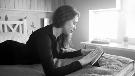 Black and white portrait of smiling businesswoman lying on bed and working on digital tablet computerの写真素材
