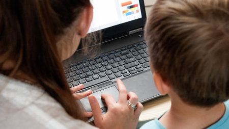 Rear view of mother with little son sitting behind laptop and studying. CHild using computer for education and learningの写真素材