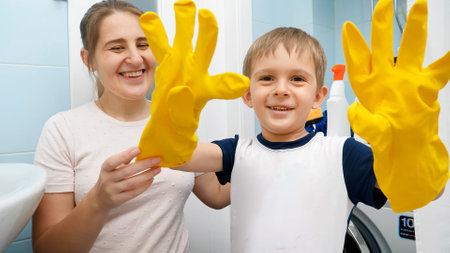 Funny laughing boy wearing yellow rubber gloves laughing and making faces before doing housewrok and cleaning bathroom with his mother. Family foing housework and having funの写真素材
