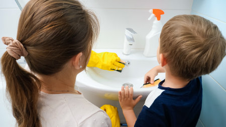 Smiling little boy helping his mother washing and cleaning bathroom at home. Child and adult doing houseworkの写真素材