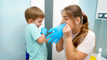 Smiling mother having fun with her toddler son while putting on protective rubber gloves before cleaning and washing bathroomの写真素材