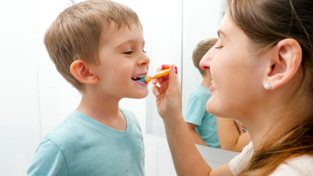 Young caring mother brushing and cleaning teeth of her little son. Parents and children taking care of teeth health and hygieneの写真素材