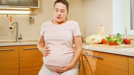 Tired pregnant woman with pain and ache in belly sitting on chair and resting after doing housework...