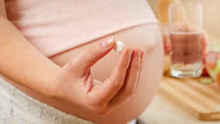 CLoseup of pregnant woman holding glss of water and medical pill or vitamins in hand. Concept of healthy lifestyle, nutrition and hydration during pregnancyの写真素材