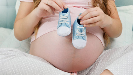 CLoseup of pregnant woman waiting for baby boy holding small baby boots in hands. Concept of...