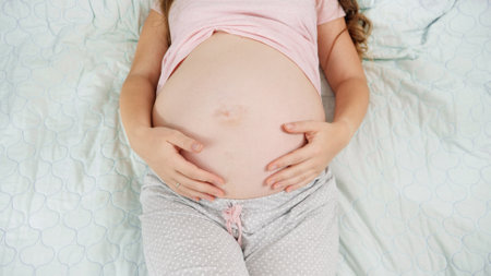 Top view of pregnant woman lying on hospital bed touching and stroking her big belly. Concept of...