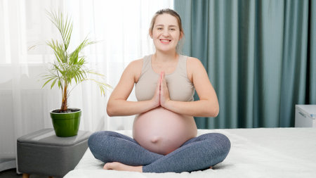 Portrait of smiling pregnant woman practicing yoga and looking in camera. Concept of healthy lifestyle, healthcare and sports during pregnancyの写真素材