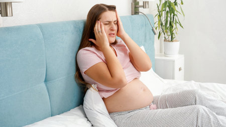 Portrait of young pregnant woman suffering from headache lying in bed. Concept of healthcare and pain during pregnancyの写真素材