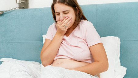 Portrait of sick pregnant woman feeling nausesa and coughing while lying in bed at morning. Healthcare and intoxication during pregnancyの写真素材