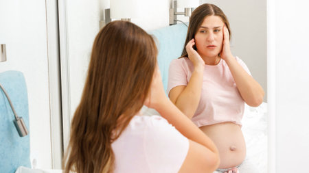 Portrait of pregnant woman suffering from head ache looking in her reflection in mirror. Concept of pregnancy healthcare and medical examination.の写真素材
