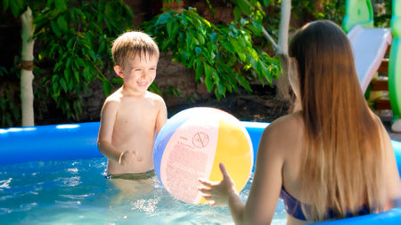 Happy laughing mother with little son playing with colorful beach ball in swimming pool. Family...