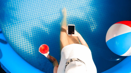Top view of young woman relaxing and lying in swimming pool and drinking cocktail while using smartphone. Concept of happy summer holidays and vacationの写真素材